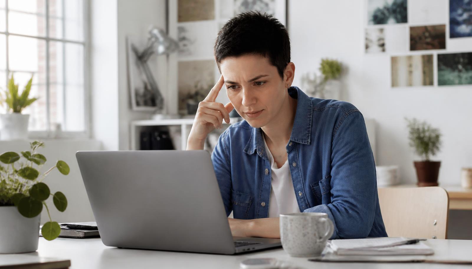 Person at a bright studio desk looking carefully at a laptop screen
